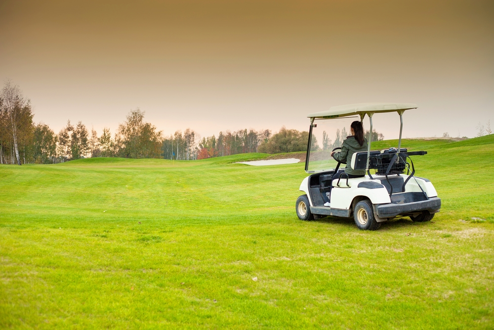 A person driving down the fairway in a golf cart during the golden hour.